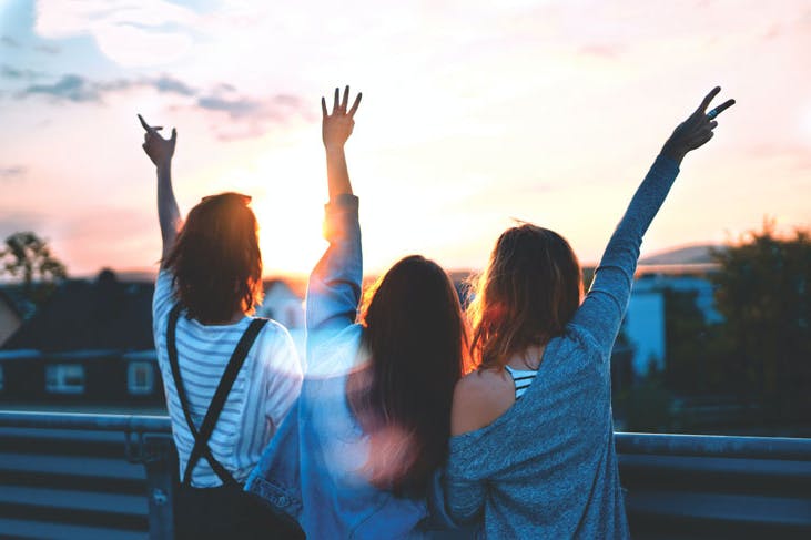 Three people throwing peace signs to a sunset at a party.